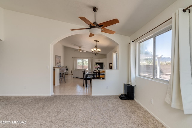 carpeted empty room featuring baseboards, arched walkways, ceiling fan with notable chandelier, and lofted ceiling