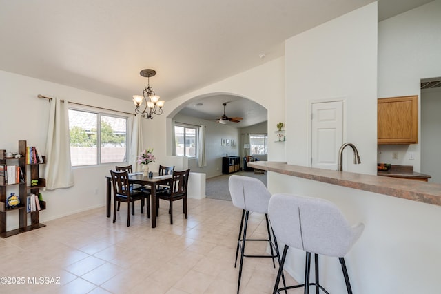 dining room with arched walkways, baseboards, high vaulted ceiling, ceiling fan with notable chandelier, and light tile patterned flooring