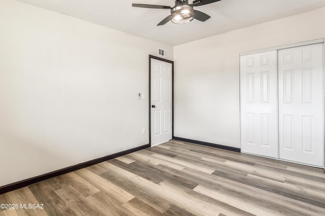 unfurnished bedroom featuring ceiling fan, visible vents, a closet, baseboards, and wood finished floors