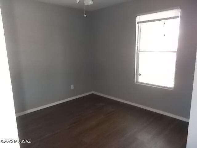 empty room featuring dark wood-style flooring, ceiling fan, and baseboards