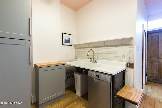 kitchen featuring stainless steel dishwasher, gray cabinetry, decorative backsplash, and light wood-style floors