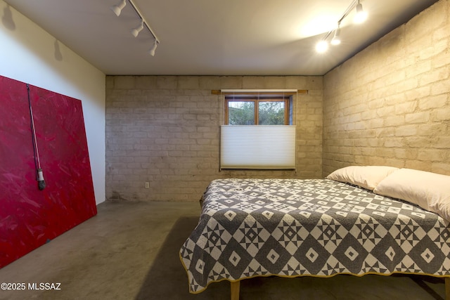 bedroom featuring track lighting, carpet floors, and brick wall