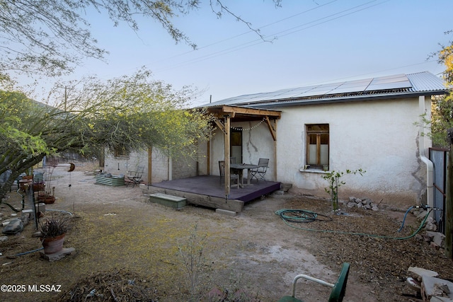 back of property featuring metal roof, a wooden deck, solar panels, and stucco siding