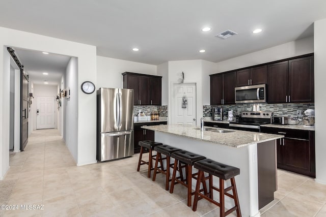 kitchen featuring decorative backsplash, a sink, stainless steel appliances, dark brown cabinetry, and a kitchen bar