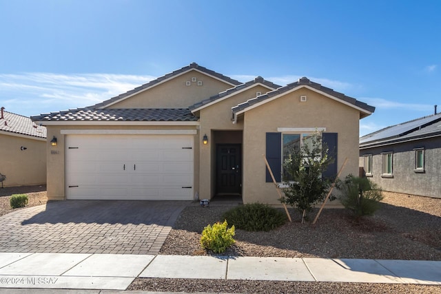 ranch-style house featuring stucco siding, decorative driveway, a tile roof, and a garage