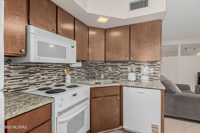 kitchen featuring a sink, visible vents, light stone counters, backsplash, and white appliances