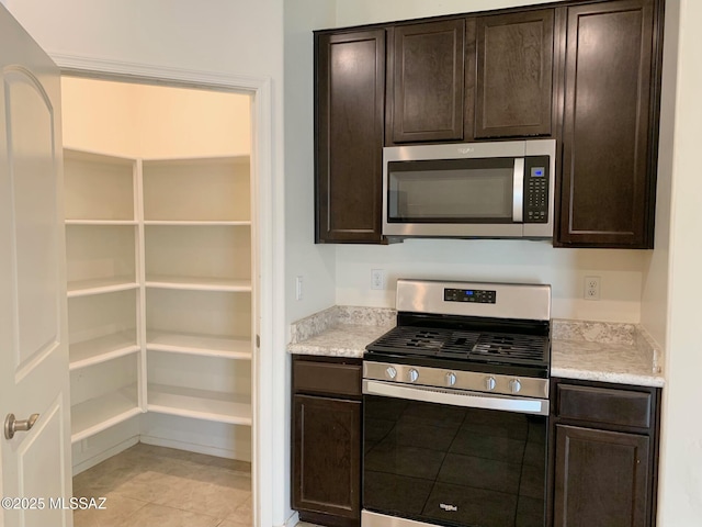 kitchen with appliances with stainless steel finishes, light tile patterned floors, and dark brown cabinetry