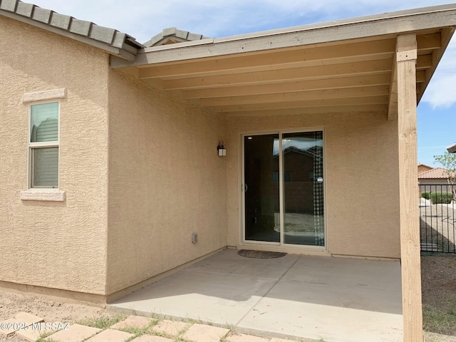 view of exterior entry featuring a patio, stucco siding, and fence