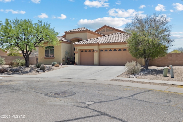 mediterranean / spanish house featuring a tile roof, fence, concrete driveway, an attached garage, and stucco siding