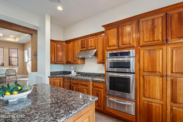 6340 N Placita Alta Reposa, Tucson, AZ 85750 - kitchen with brown cabinetry, stainless steel appliances, under cabinet range hood, a warming drawer, and light tile patterned flooring