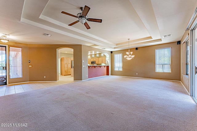 unfurnished living room featuring arched walkways, light colored carpet, ceiling fan with notable chandelier, visible vents, and a raised ceiling