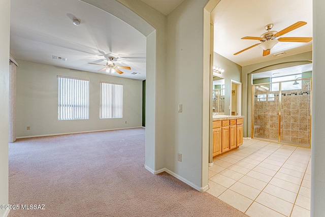 empty room with visible vents, arched walkways, a ceiling fan, and light colored carpet