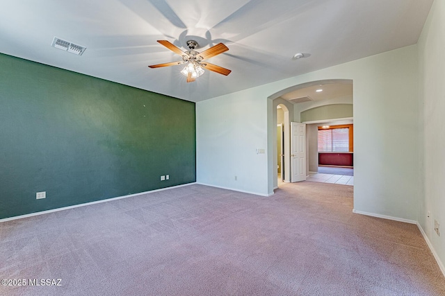 carpeted empty room with visible vents, a ceiling fan, baseboards, and arched walkways