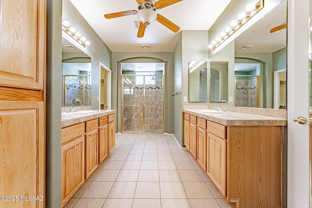 bathroom with tile patterned floors, two vanities, a shower stall, and a ceiling fan