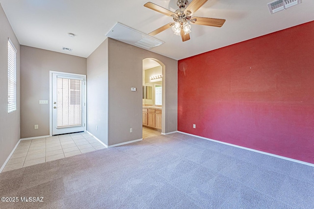 empty room with ceiling fan, visible vents, light carpet, baseboards, and arched walkways