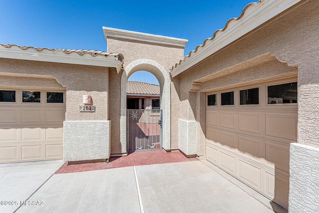 view of exterior entry featuring stucco siding, a tiled roof, and concrete driveway