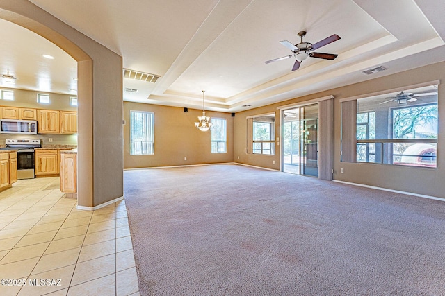 unfurnished living room with baseboards, ceiling fan with notable chandelier, light colored carpet, and a tray ceiling