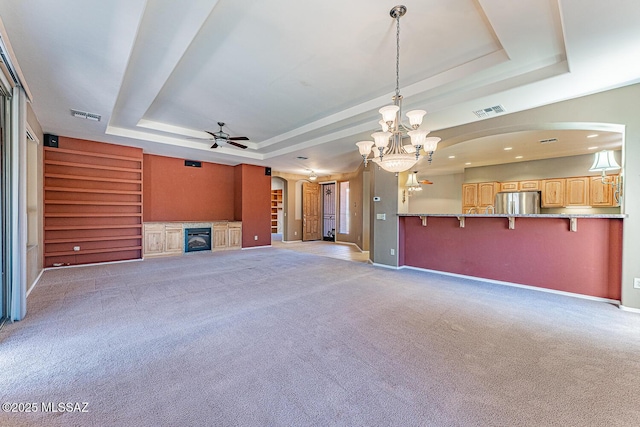 unfurnished living room with arched walkways, a raised ceiling, and ceiling fan with notable chandelier