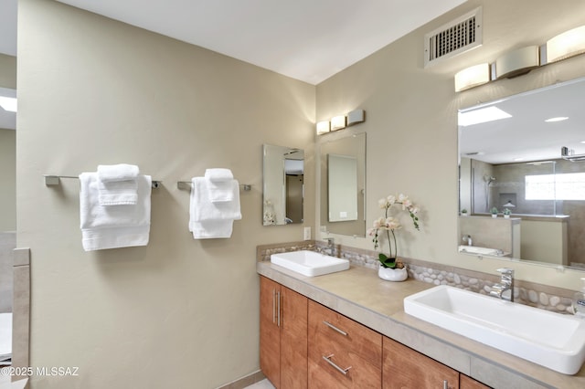 full bath with double vanity, visible vents, a tile shower, and a sink