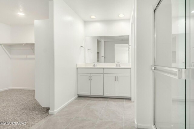bathroom with double vanity, a shower stall, a spacious closet, and baseboards