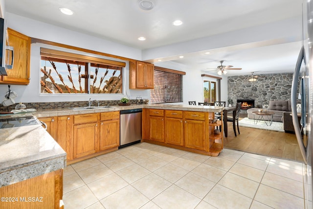 kitchen with stainless steel appliances, a sink, a stone fireplace, a peninsula, and ceiling fan