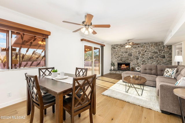 dining area with a ceiling fan, a stone fireplace, light wood-type flooring, baseboards, and ornamental molding
