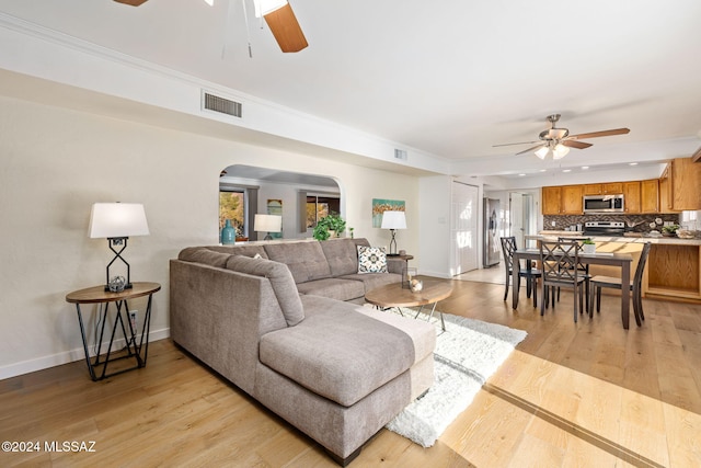 living area with a ceiling fan, arched walkways, baseboards, and light wood-style flooring