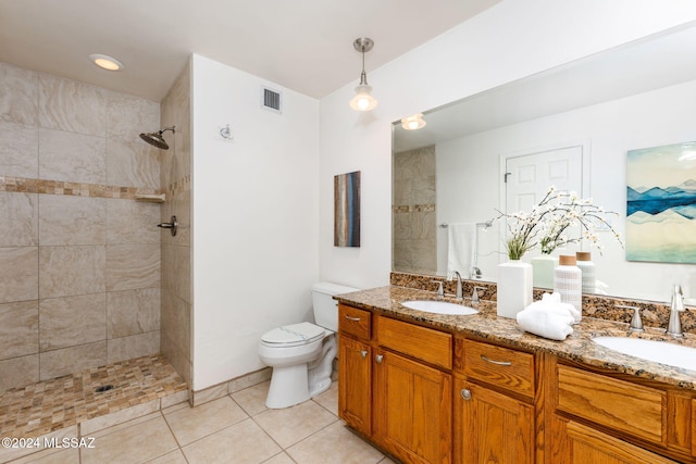 bathroom with a tile shower, tile patterned flooring, double vanity, and toilet