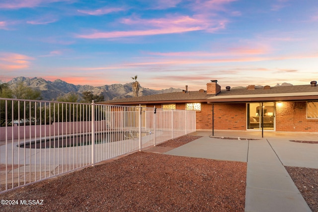 back of property at dusk featuring a patio area, a fenced backyard, a mountain view, brick siding, and a chimney