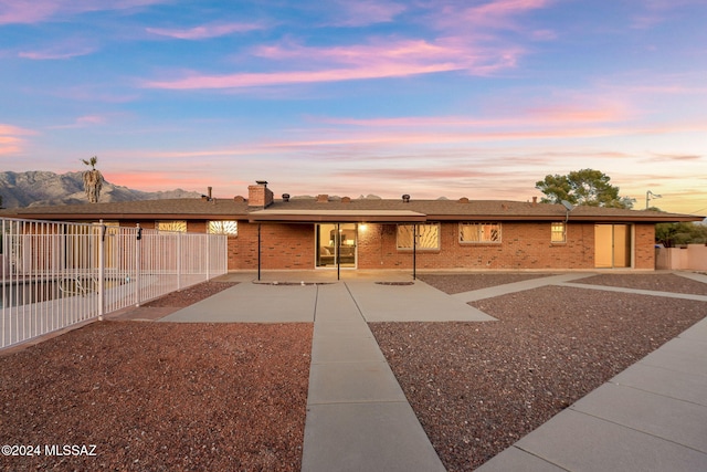 view of front of house featuring a patio, brick siding, fence, a mountain view, and a chimney