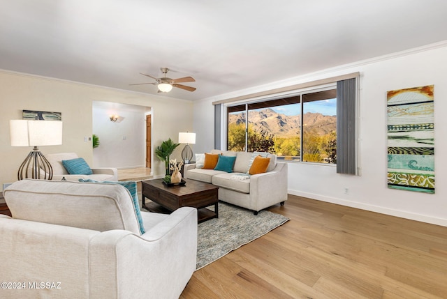 living area with crown molding, light wood-style flooring, baseboards, a ceiling fan, and a mountain view