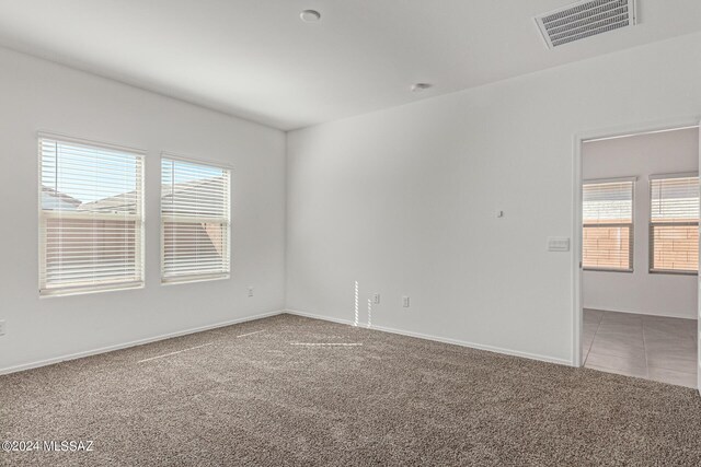 spare room featuring carpet, visible vents, plenty of natural light, and baseboards