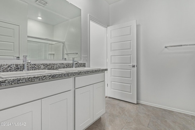 bathroom featuring double vanity, a sink, a shower with door, and baseboards