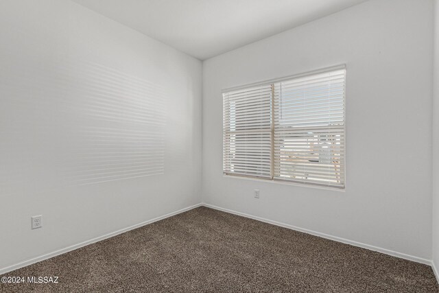 spare room with baseboards and dark carpet