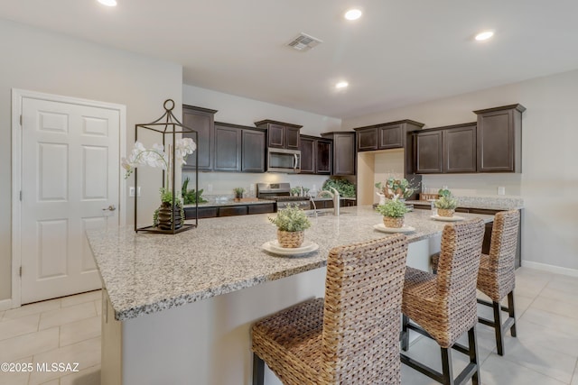 kitchen with light stone countertops, light tile patterned floors, dark brown cabinetry, visible vents, and appliances with stainless steel finishes