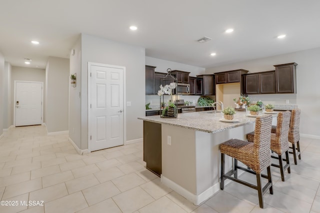 kitchen with a sink, stainless steel appliances, dark brown cabinetry, light stone countertops, and recessed lighting