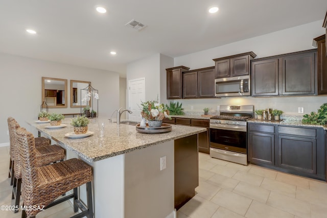 kitchen with a sink, visible vents, light stone counters, and stainless steel appliances