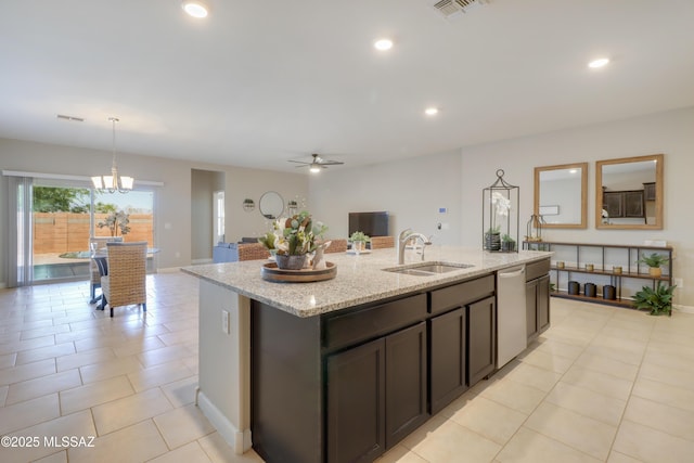 kitchen with stainless steel dishwasher, a sink, visible vents, light stone countertops, and a kitchen island with sink