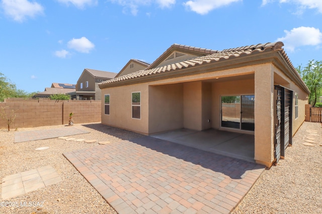 rear view of house featuring a tile roof, stucco siding, a fenced backyard, and a patio area