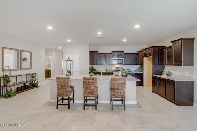 kitchen featuring stove, dark brown cabinetry, an island with sink, recessed lighting, and stainless steel microwave