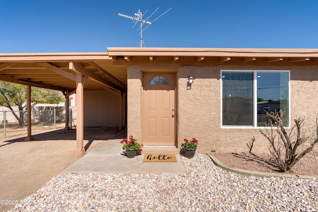 view of exterior entry featuring stucco siding and fence