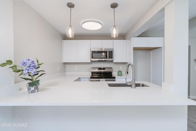 kitchen featuring pendant lighting, a peninsula, white cabinetry, a sink, and appliances with stainless steel finishes