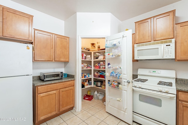 kitchen with a toaster, dark countertops, light tile patterned floors, and white appliances