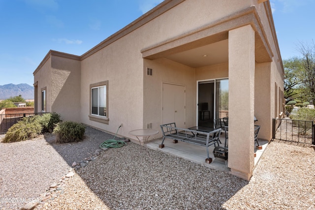 back of property with a mountain view, stucco siding, fence, visible vents, and a patio area