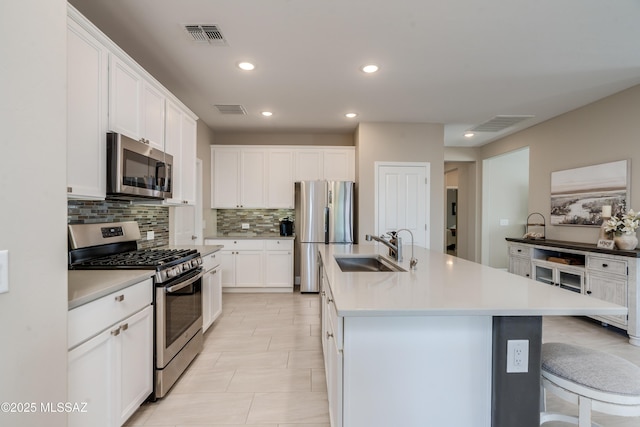 kitchen featuring appliances with stainless steel finishes, a sink, a kitchen island with sink, tasteful backsplash, and visible vents
