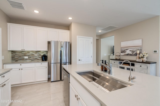 kitchen featuring white cabinets, appliances with stainless steel finishes, a sink, decorative backsplash, and visible vents