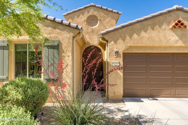 entrance to property with concrete driveway, stucco siding, an attached garage, and a tiled roof