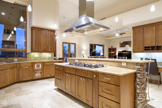 kitchen featuring brown cabinetry, a breakfast bar area, a large island, island exhaust hood, and stainless steel gas stovetop