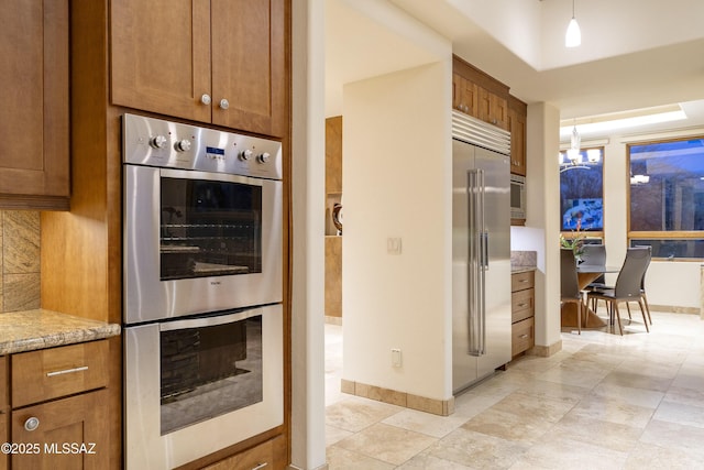 kitchen featuring brown cabinetry, appliances with stainless steel finishes, and light stone counters