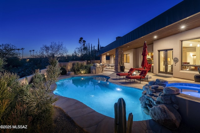 pool at night featuring area for grilling, an in ground hot tub, a fenced in pool, fence, and a patio